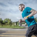 Caucasian man jogging on a city street crosswalk wearing a blue t-shirt and yellow watch.